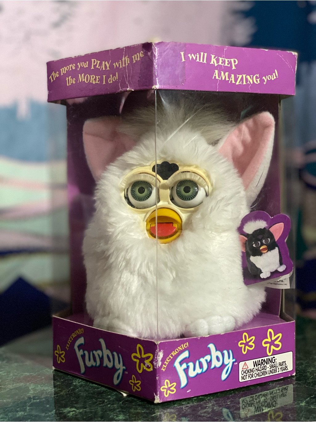 Boxed first-generation 1998 Furby with white and pink fur and mechanical eyes, in its original purple Tiger Electronics box